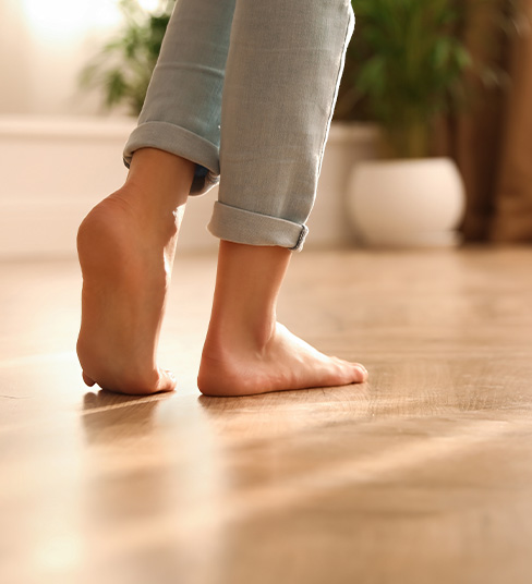 Barefoot person standing on polished wooden floor, showcasing warmth and comfort in the home.