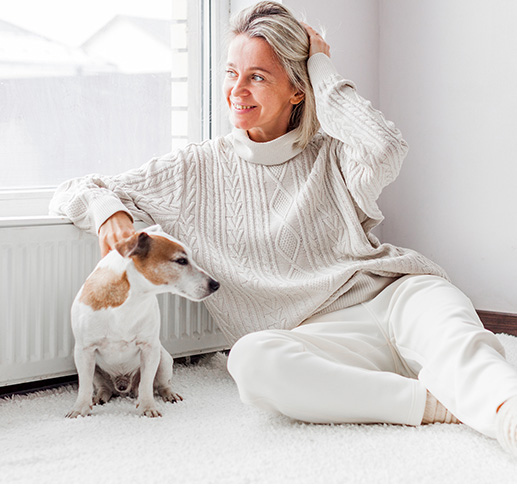 Woman relaxing beside a radiator with a small dog on a cozy rug.