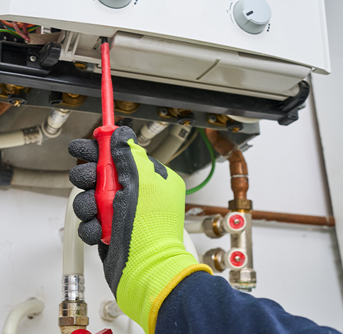 Hand adjusting a boiler valve with a red screwdriver and wearing a safety glove.