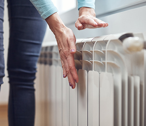 Person checking the warmth of a radiator in a home setting.