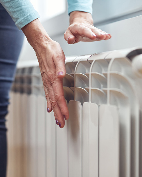 Hands gently touching a radiator for warmth and comfort.